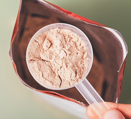 ملعقة قياس بروتين مصل اللبن عن قرب فوق كيس مفتوح على خلفية خضراء، منظر علوي